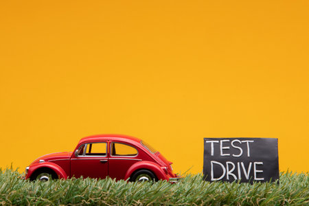 Chisinau, Moldova - August 15th 2019: A red car figurine aligned to the left on grass next to a blue sign with the words test drive on it, on orange background.のeditorial素材