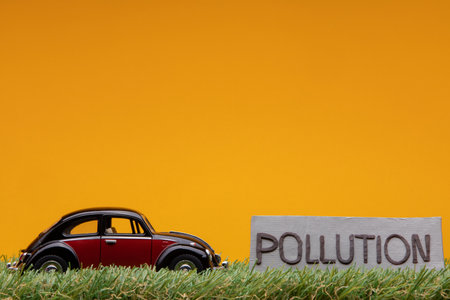 Chisinau, Moldova - August 15th 2019: A crimson car figurine aligned to the left on grass next to a gray sign with the word pollution on it, on orange background.のeditorial素材