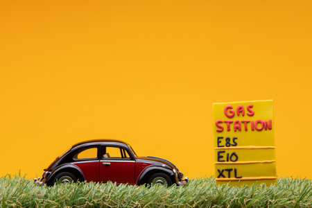 Chisinau, Moldova - August 15th 2019: A crimson car figurine aligned to the left on grass next to an yellow gas station sign.のeditorial素材