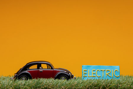 Chisinau, Moldova - August 15th 2019: A crimson car figurine aligned to the left on grass next to a pale blue sign with the word electric on it, on orange background.のeditorial素材