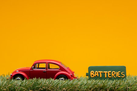 Chisinau, Moldova - August 15th 2019: A red car figurine aligned to the left on grass next to a green sign with the word batteries on it, on orange background.のeditorial素材