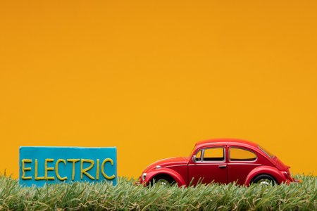 Chisinau, Moldova - August 15th 2019: A red car figurine aligned to the right on grass next to a pale blue sign with the word electric on it, on orange background.のeditorial素材