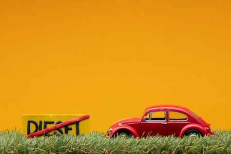 Chisinau, Moldova - August 15th 2019: A red car figurine aligned to the right on grass next to an yellow sign with the word diesel cut on it, on orange background.のeditorial素材