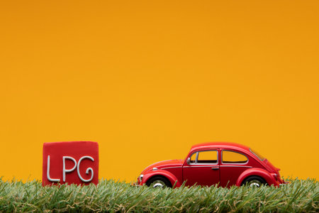 Chisinau, Moldova - August 15th 2019: A red car figurine aligned to the right on grass next to a red sign with the word LPG on it, on orange background.のeditorial素材