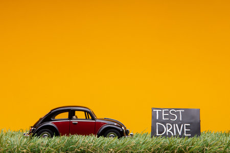 Chisinau, Moldova - August 15th 2019: A crimson car figurine aligned to the left on grass next to a blue sign with the words test drive on it, on orange background.のeditorial素材