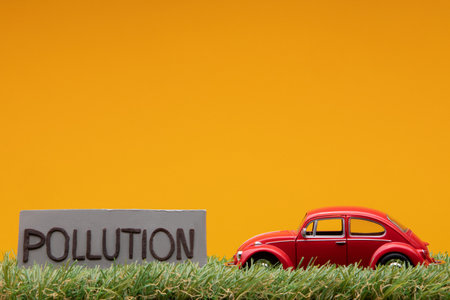 Chisinau, Moldova - August 15th 2019: A red car figurine aligned to the right on grass next to a gray sign with the word pollution on it, on orange background.のeditorial素材