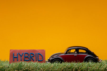 Chisinau, Moldova - August 15th 2019: A crimson car figurine aligned to the right on grass next to a red sign with the word hybrid on it, on orange background.のeditorial素材