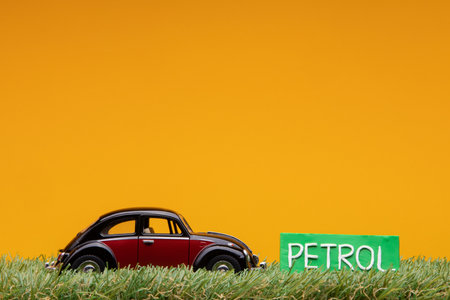 Chisinau, Moldova - August 15th 2019: A crimson car figurine aligned to the left on grass next to a green sign with the word petrol on it, on orange background.のeditorial素材