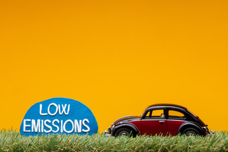 Chisinau, Moldova - August 15th 2019: A crimson car figurine aligned to the right on grass next to a pale blue sign with the words low emissions on it, on orange background.のeditorial素材