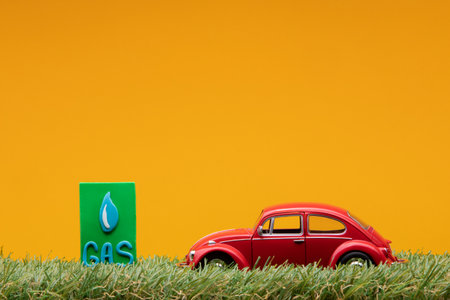Chisinau, Moldova - August 15th 2019: A red car figurine aligned to the right on grass next to a green sign with the word gas on it, on orange background.のeditorial素材