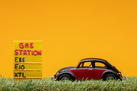 Chisinau, Moldova - August 15th 2019: A crimson car figurine aligned to the right on grass next to an yellow gas station sign.のeditorial素材