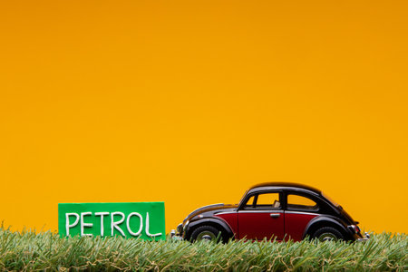 Chisinau, Moldova - August 15th 2019: A crimson car figurine aligned to the right on grass next to a green sign with the word petrol on it, on orange background.のeditorial素材
