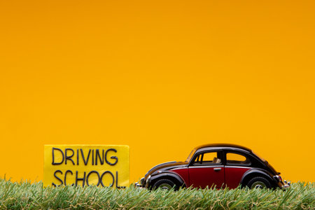 Chisinau, Moldova - August 15th 2019: A crimson car figurine aligned to the right on grass next to an yellow sign with the words driving school on it, on orange background.のeditorial素材