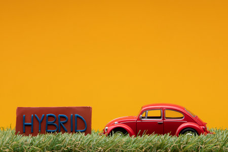 Chisinau, Moldova - August 15th 2019: A red car figurine aligned to the right on grass next to a red sign with the word hybrid on it, on orange background.のeditorial素材