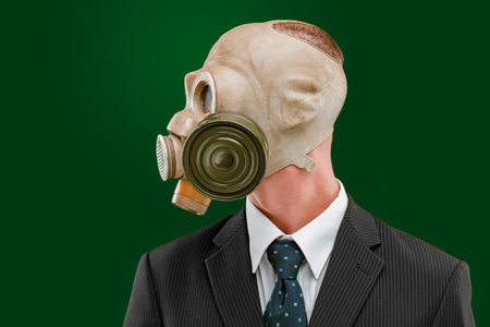 Portrait of a man looking to the left, wearing a dark business suit and an old gas mask, isolated on green background.の写真素材