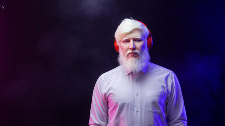 An old albino grandfather listening to music with new, red headphones, looking serious, isolated on a beautiful, colorful background.の写真素材