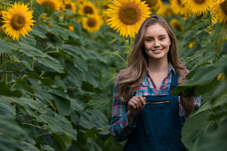 Gorgeous young female farmer walking through the middle of a green sunflower field during a sunny, beautiful day.の写真素材