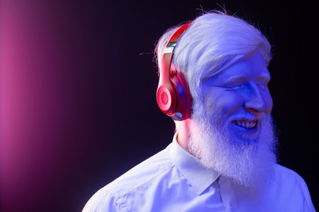 An old albino grandfather enjoying to music with new, red headphones, smiling, isolated on a beautiful, colorful background.の写真素材
