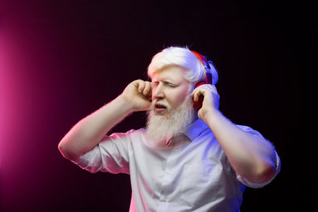 An old albino grandfather enjoying to music with new, red headphones, isolated on a beautiful background.の写真素材