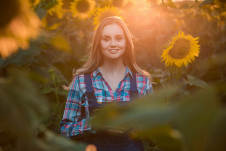 Gorgeous young female farmer standing in the middle of a sunflower field, during a majestic sunrise...