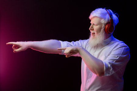 An old albino grandfather enjoying to music with new, red headphones, isolated on a beautiful background.の写真素材