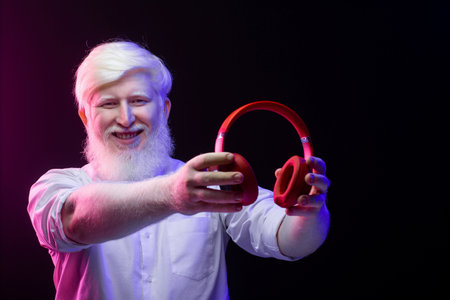 An old albino man holding a pair of new, red headphones, isolated on a beautiful, colorful background.の写真素材