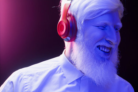 An old albino grandfather enjoying to music with new, red headphones, smiling, isolated on a beautiful, colorful background.の写真素材