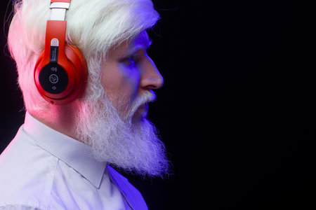 An old albino grandfather listening to music with new, red headphones, looking to the right,...