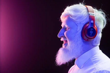 An old albino grandfather enjoying to music with new, red headphones, smiling, isolated on a beautiful, colorful background.の写真素材