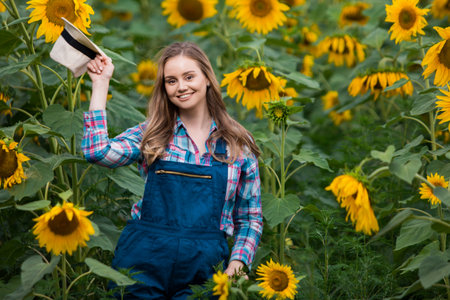 Gorgeous young female farmer standing in the middle of a green sunflower field, during a sunny, beautiful day.の写真素材