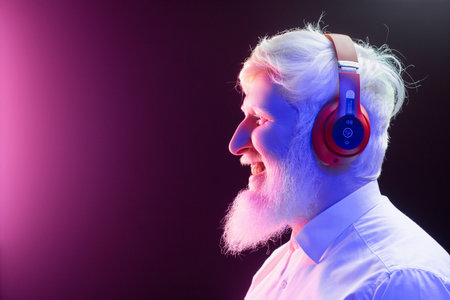 An old albino grandfather enjoying to music with new, red headphones, smiling, isolated on a beautiful, colorful background.の写真素材