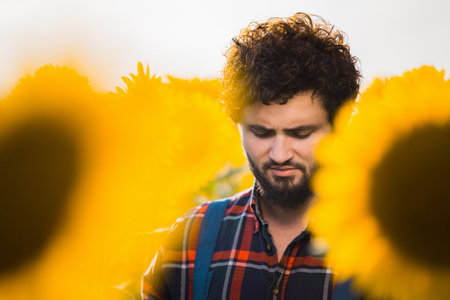 Handsome young farmer standing in the middle of a golden sunflower field holding his tablet during a sunny, beautiful day, shot upfront, closeup.の写真素材