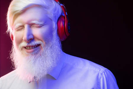 An old albino grandfather listening to music with new, red headphones, smiling, isolated on a beautiful, colorful background.の写真素材