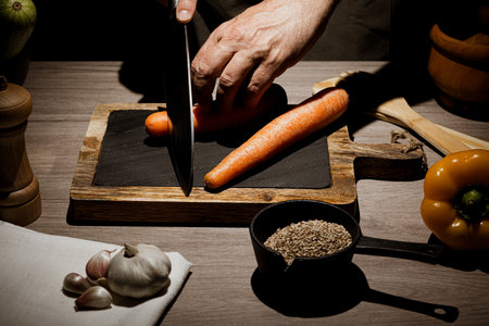 a person cuts some vegetables with a knife in a kitchen on a stone and wood table. cut carrots.