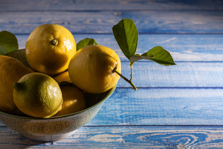 close up of bowl full of lemons on blue wooden table with nice sunrise light coming through windowの写真素材