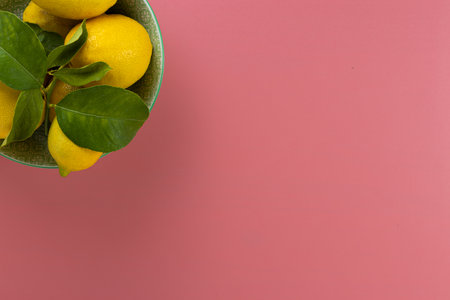 Overhead shot of a bowl full of fresh organic lemons with their green leaves on a pink tableの写真素材