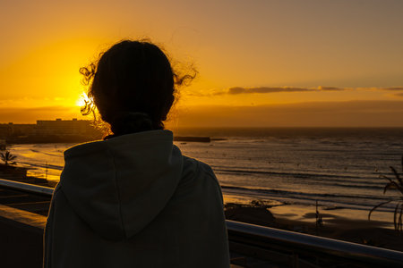 Woman looking at the sunset on the beach of Ponta Delgadaの写真素材