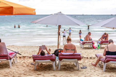 BORACAY ISLAND, PHILIPPINES - November 17, 2017 : People on sunbed reading book under parasol at tropical islandのeditorial素材