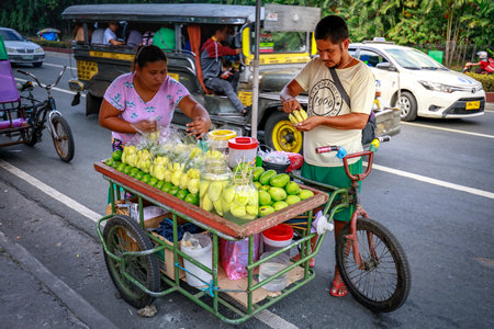 Manila, Philippines - Feb 4, 2018 : A street food vendor slices fresh green mango which sells on food cart at a sidewalk along a street in Manila city, Philippines.のeditorial素材