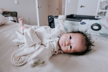 Cute asian baby boy lying on bed at morning home. Baby looking at the camera.の写真素材