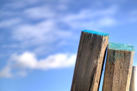 A couple of posts leaning against a fence, with a blue sky in the background.の写真素材