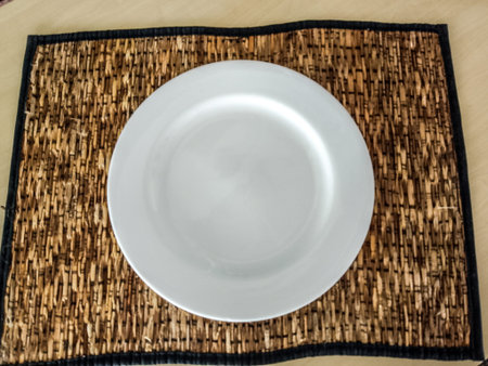 Top view of empty white ceramic plate on rustic woven placemat.の写真素材