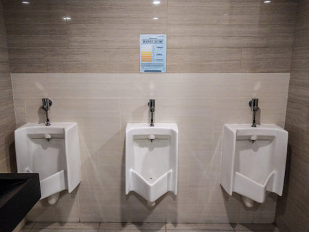 Row of modern white ceramic urinals in a clean public restroom with health poster on the wall.