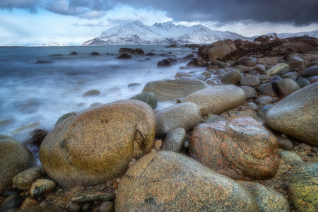 Stones at beach of northern Norway. In background snow-capped peaks of cold end of the world mountainsの写真素材