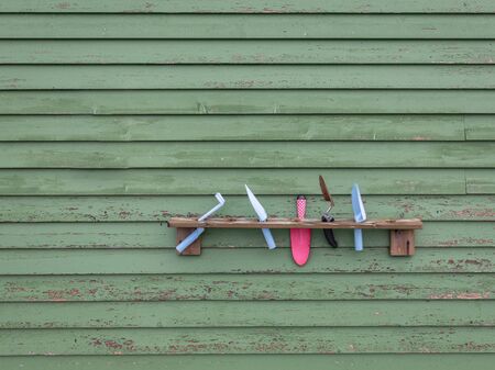 Garden tools on wooden shelf hanging on green wall made from painted planks. Colorful, plastic shovels, spades isolated from background.の写真素材