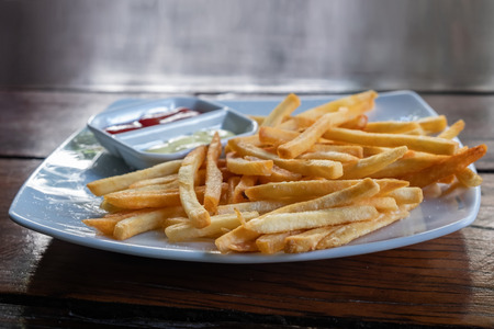 Homemade French Fries with potato sauce and mayonnaise on white plate and wood table background