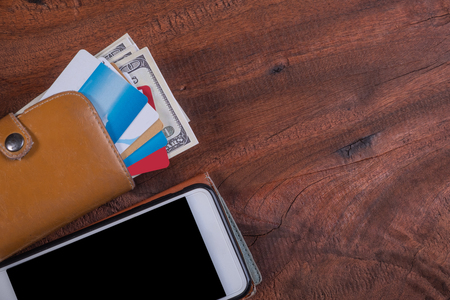Credit cards and money in wallet put on a smart phone and wood background
