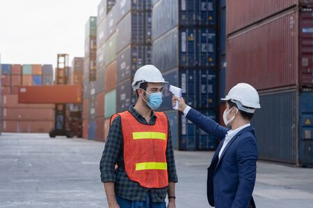 New normal concept,Engineer check the staff integrity by measuring the temperature,wear mask and helmet before working in factory or warehouse area Prevent accident from work or dust and Coronavirusの写真素材