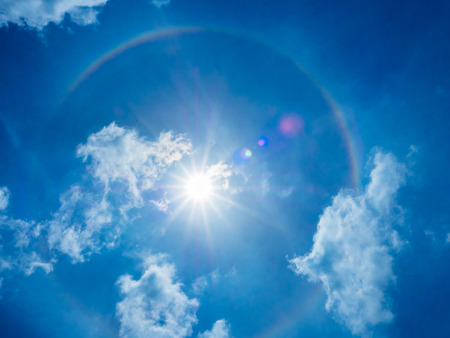The phenomenon of the sun halo is showing with the flare behind the blue clear and little cloud sky. It occured by the refraction of the sunlight with moisture in the innermost atmosphere.の写真素材