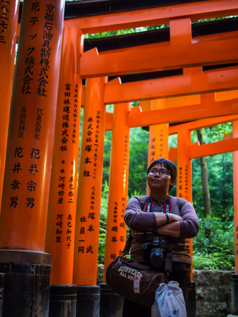 Kyoto, Japan - Jun 5, 2016 : The woman photographer is acting with the japanese historic place in Kyoto named Fushimi Inari Taisha where these red pillars or torii are lining in pattern with letters.のeditorial素材